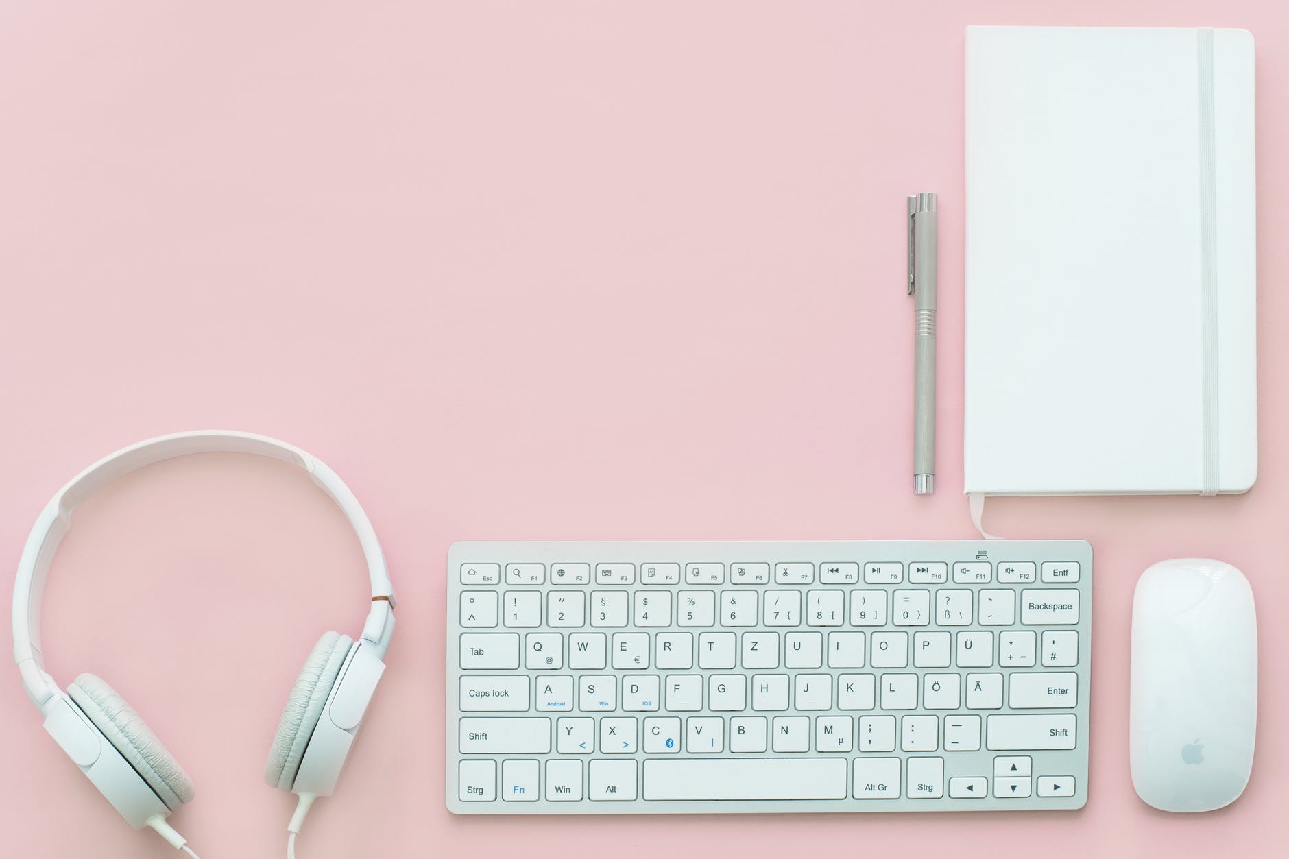 apple compact keyboard magic mouse and corded headphones on pink surface